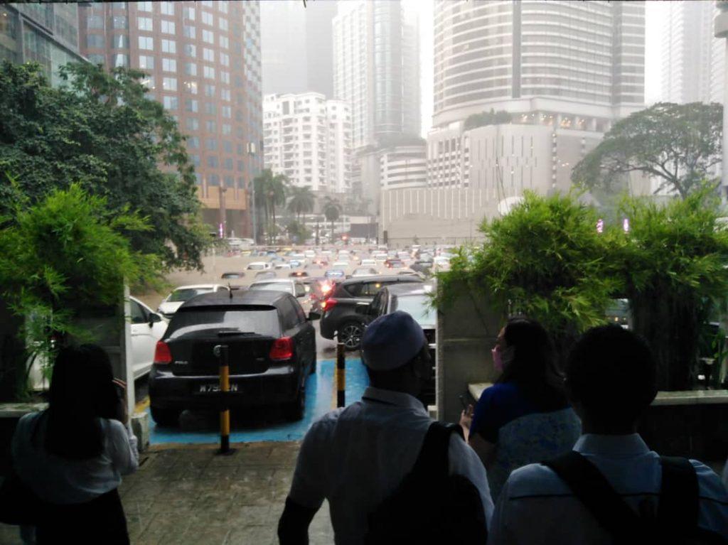 People take shelter at a building in the Kuala Lumpur city centre as heavy rain causes water levels to rise, leaving vehicles almost totally submerged.