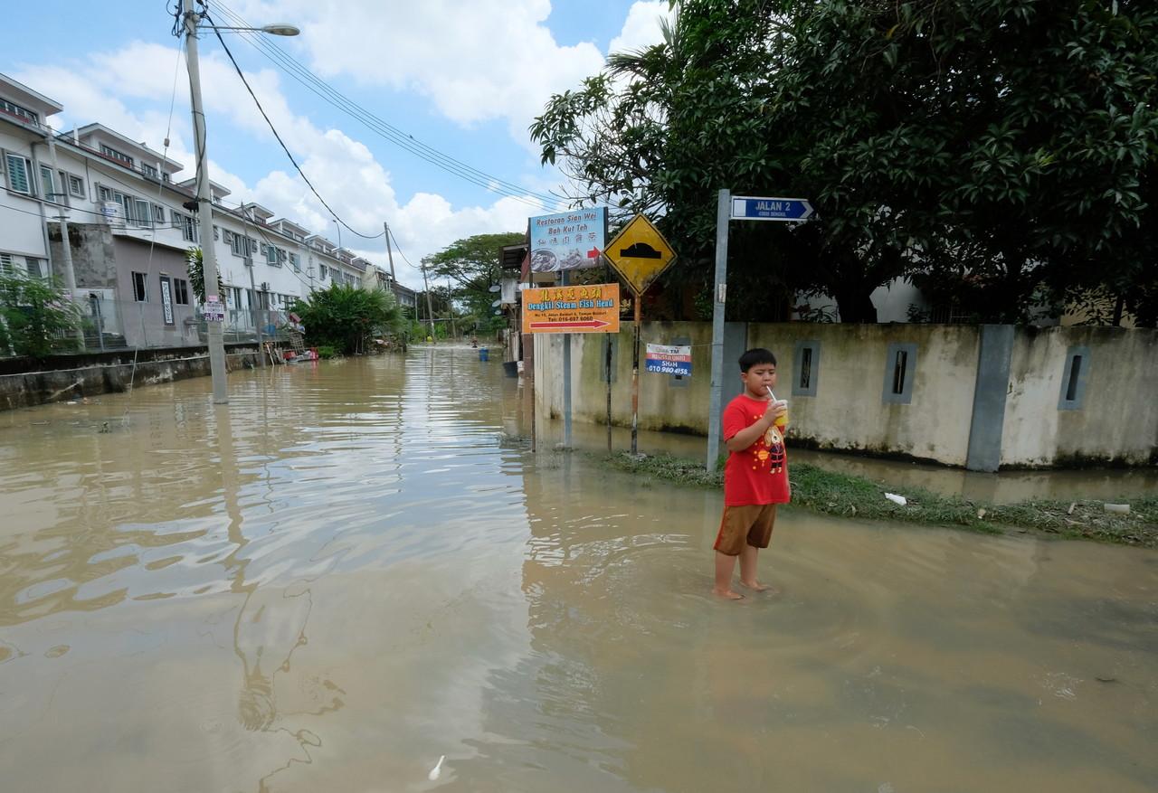 A boy holds a drink as he stands ankle-deep in floodwater at his housing area in Taman Baiduri, Dengkil, which was hit by flash floods several days ago. Photo: Bernama