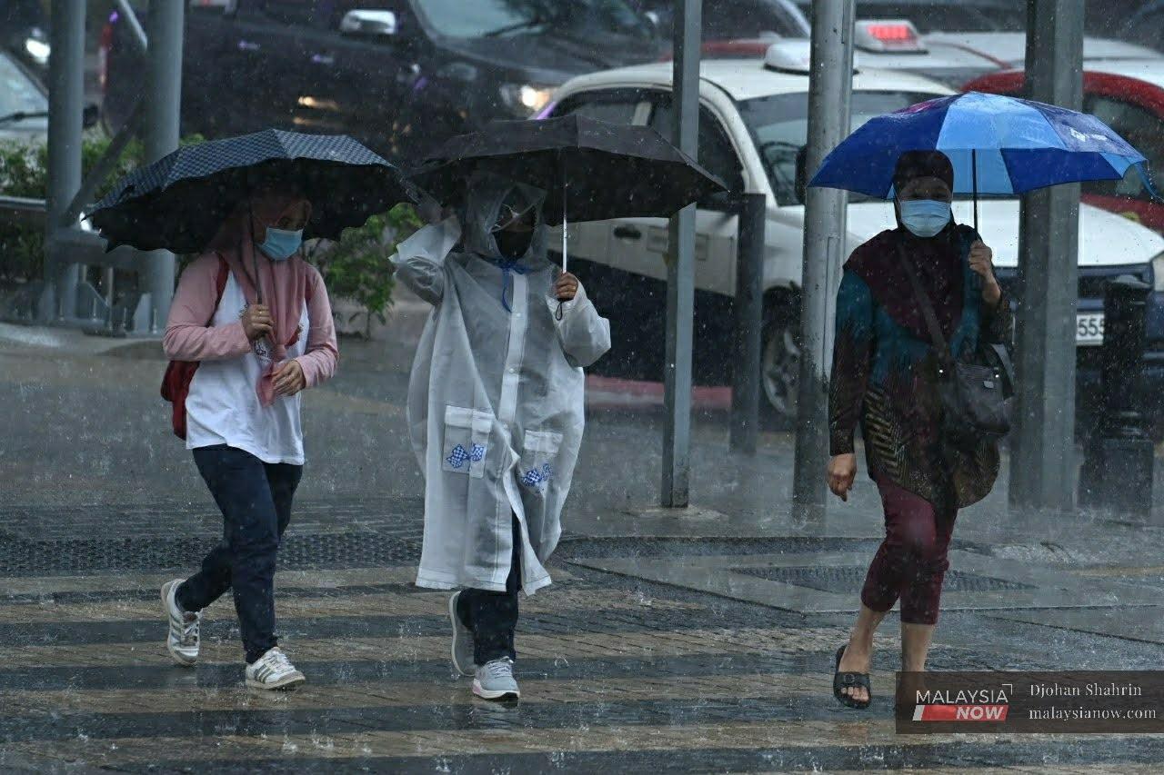Several women cross the street through heavy rain at Jalan Dang Wangi in Kuala Lumpur.
