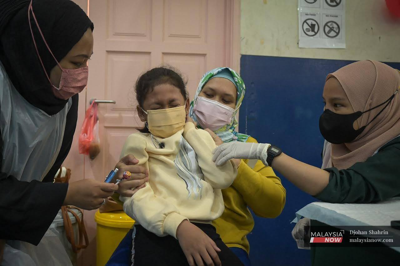 A woman comforts her child as a nurse offers her a lollipop at the Dewan Komuniti Taman Bukit Mewah vaccination centre in Kajang.