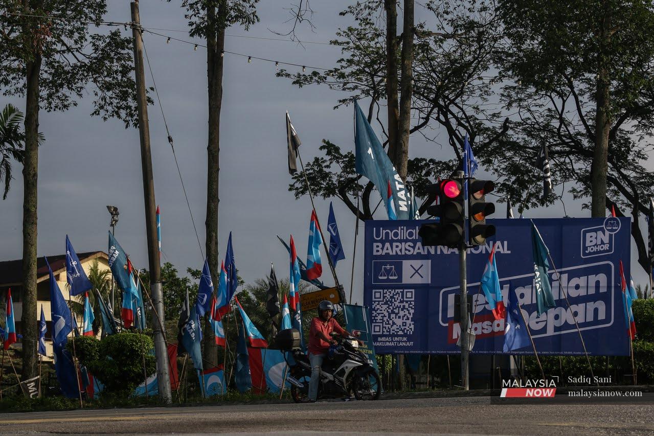A motorcyclist stops at a juntion in Kampung Melayu Majidee beside a billboard featuring Barisan Nasional and an array of party flags ahead of the state election in Johor on March 12.
