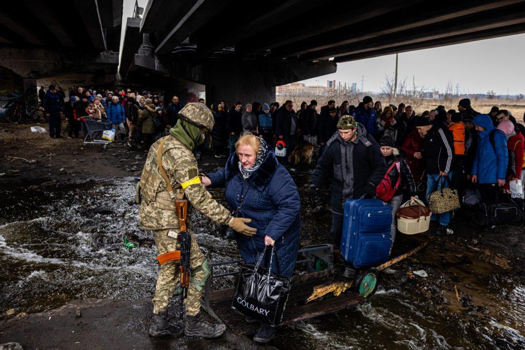 A Ukrainian serviceman helps evacuees gathered under a destroyed bridge, as they flee the city of Irpin, northwest of Kyiv, on March 7. Photo: AFP