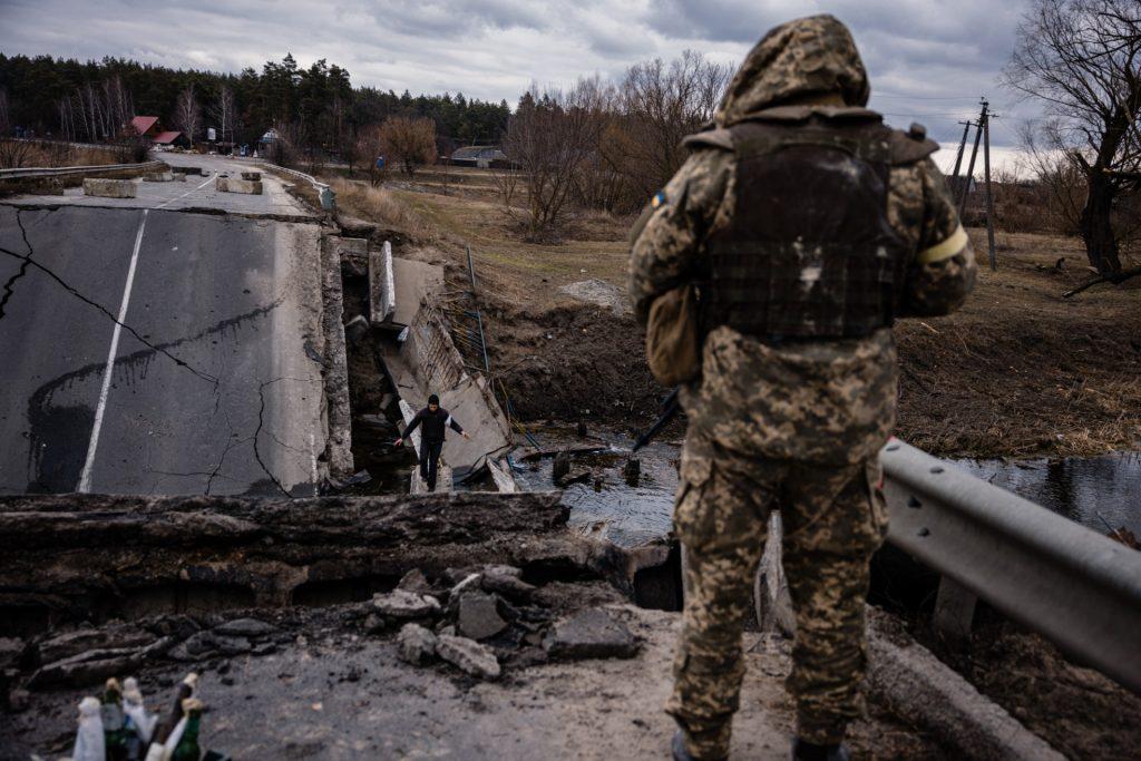 An Ukrainian serviceman looks at a civilian crossing a blown up bridge in a village, east of the town of Brovary on March 6. Photo: AFP