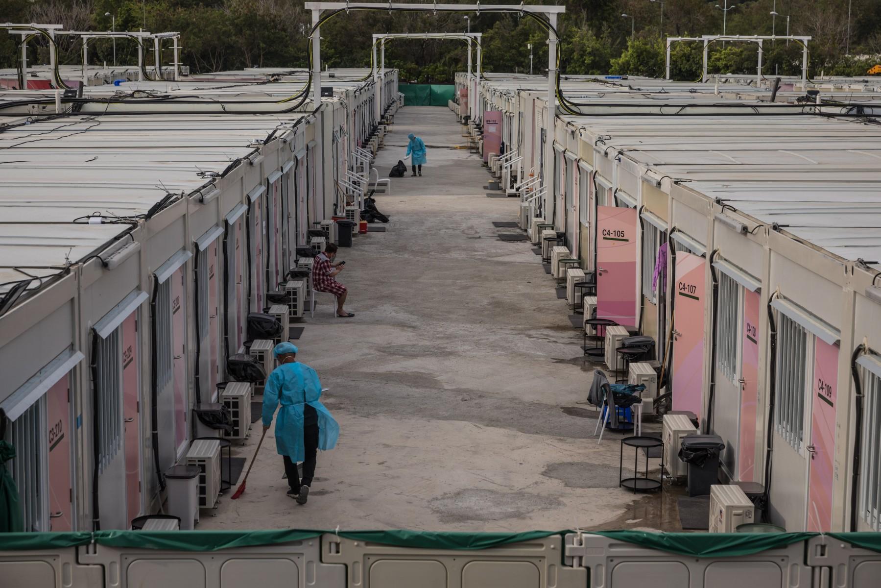 Workers wearing personal protective equipment clean next to cabins as a man (centre) uses his phone at a temporary isolation facility housing Covid-19 patients in the San Tin area of Hong Kong on March 16. Photo: AFP