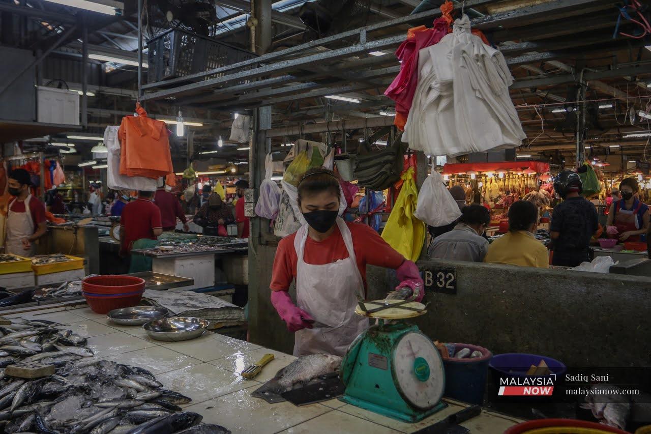 Seorang penjual memakai pelitup muka ketika sedang menyiapkan ikan yang dibeli pelanggan di Pasar Chow Kit, Kuala Lumpur.