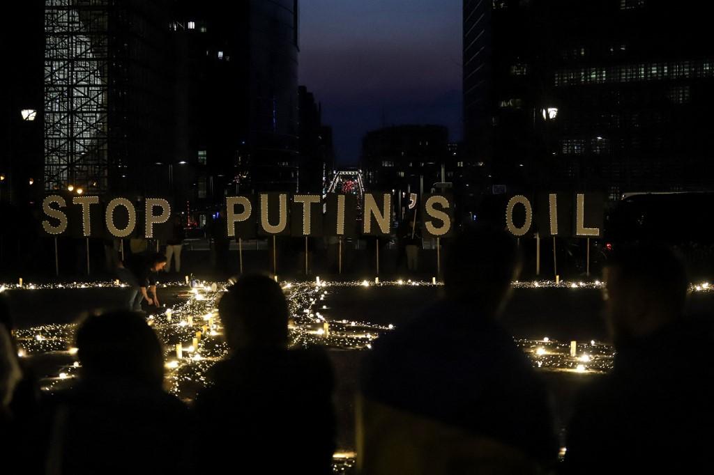 Demonstrators and activists stand in front of signs reading 'Stop Putin's oil' during a vigil for Ukraine near the European Union headquarters in Brussels, on March 22. Photo: AFP
