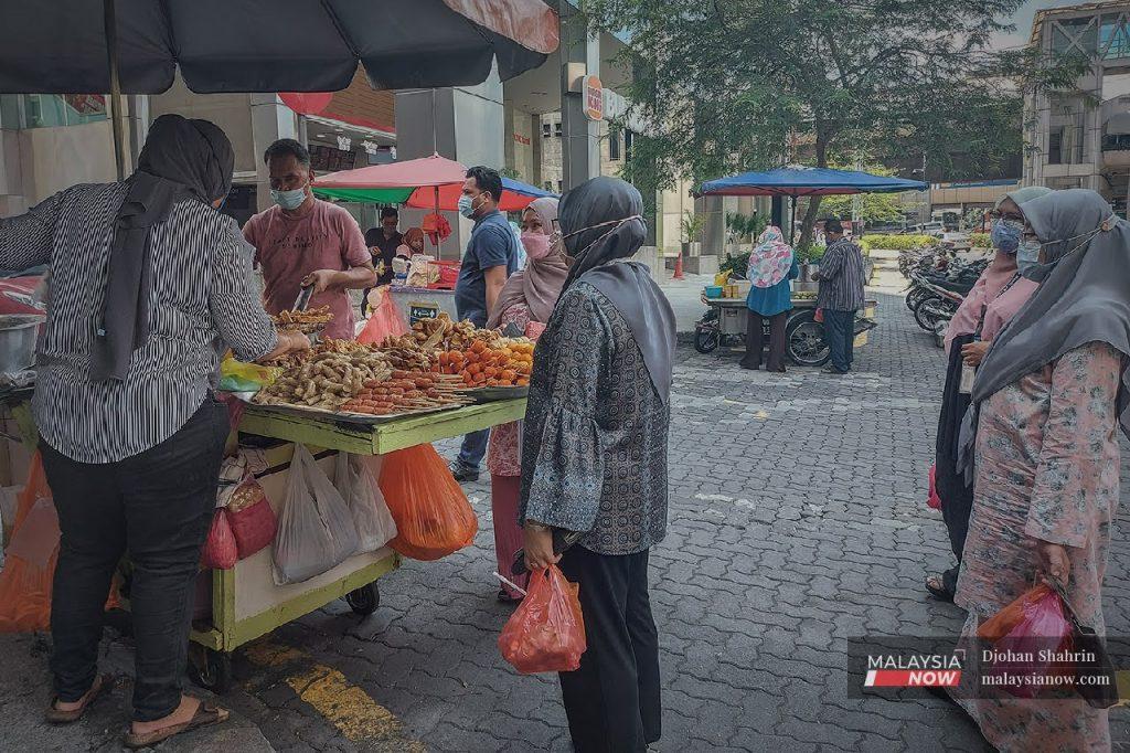 Customers wearing face masks to curb the spread of Covid-19 wait to buy lunch at a food truck in Jalan Melaka, Kuala Lumpur.