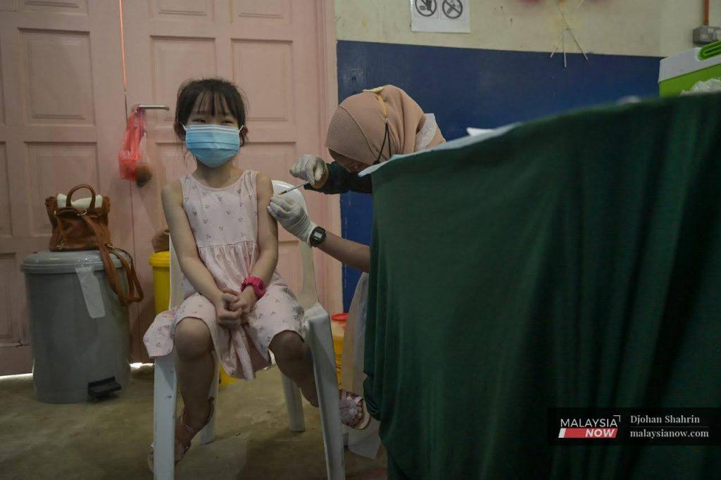 A young girl clasps her hands as a nurse administers a shot of Covid-19 vaccine for children at the Dewan Komuniti Taman Bukit Mewah vaccination centre in Kajang.