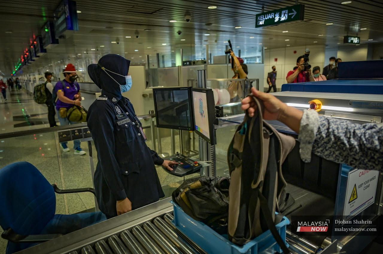 Security personnel check the luggage of travellers at KLIA in Sepang as borders reopen to international visitors today.