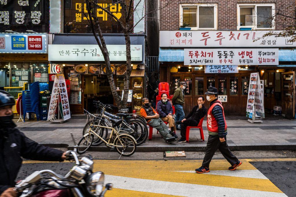 Three men chat as they sit on chairs on a pavement as a motorist drives past a pedestrian on the road in Seoul on Nov 4, 2021. Photo: AFP