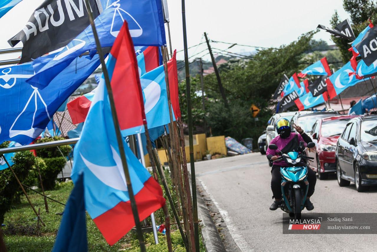 A motorcyclist holds up a peace sign as he makes his way past an array of party flags put up at Kampung Melayu Majidee ahead of the Johor state election on March 12.