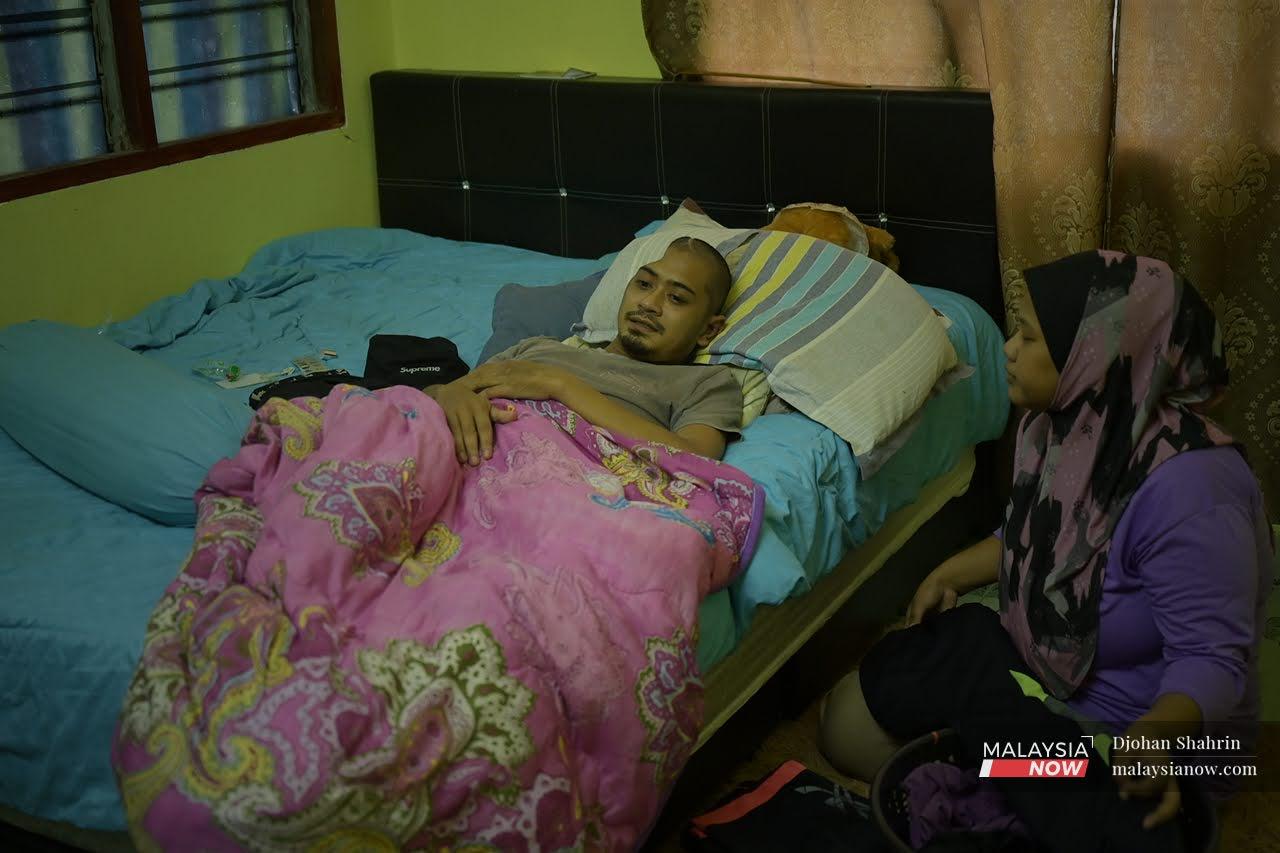 Mohd Sobrin Salleh lies in bed after his accident while his wife comforts him at his father's house in Sitiawan, Perak.