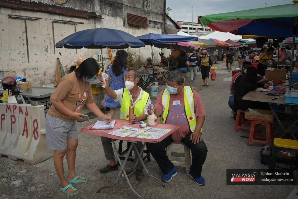 A volunteer takes a woman's temperature as she writers her details in a log book before entering the market in Ampang.