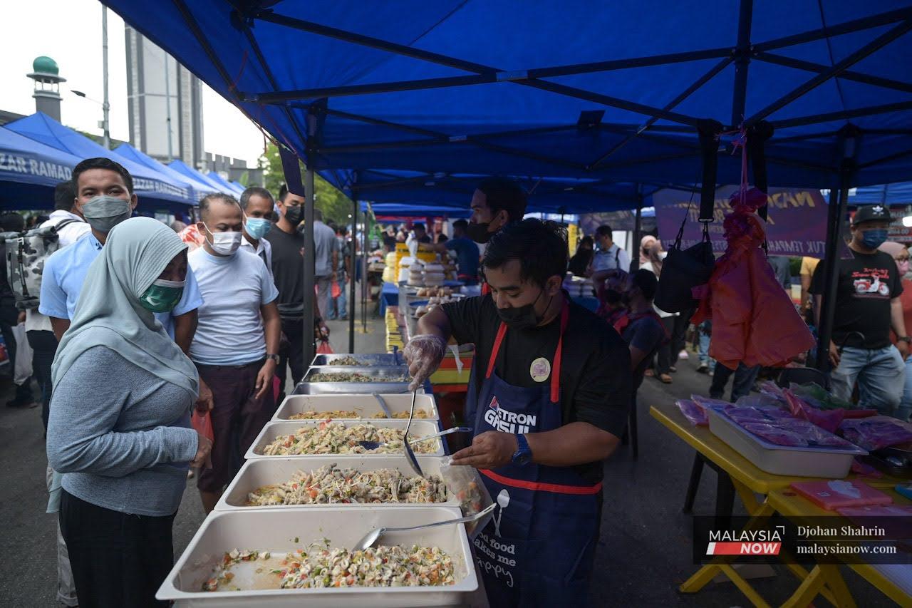 Seorang peniaga pasar Ramadan Kampung Baru memakai pelitup muka  ketika membungkus makanan yang dipesan pelanggannya.
