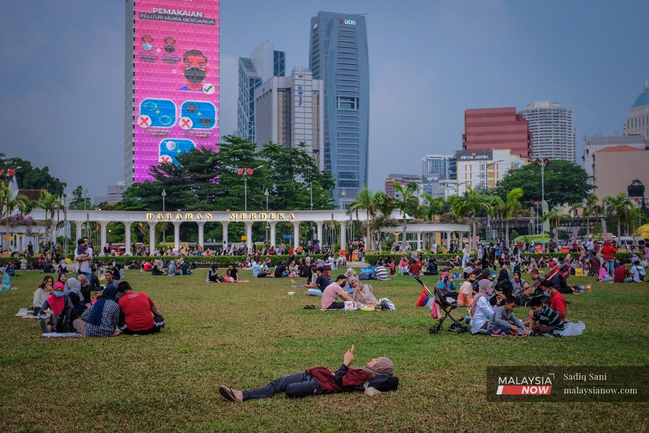 A woman looks at her phone as she lies in the middle of the field at the Sultan Abdul Samad building in Dataran Merdeka, along with others waiting for the breaking of fast.
