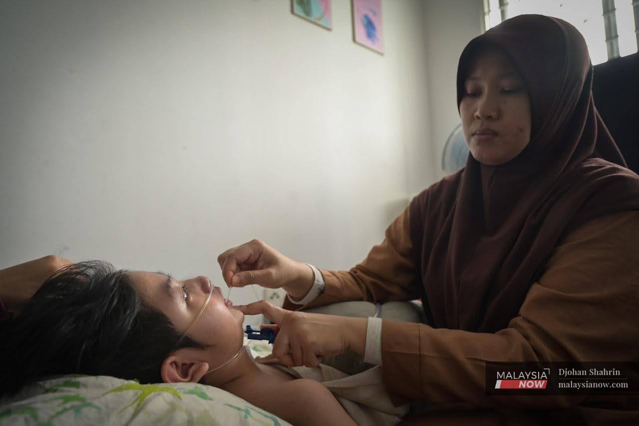 Ibu tunggal Zaitul Akma Mohd Zin, melakukan proses menyedut kahak anaknya yang menghidap penyakit neuron kronik melalui tiub yang disambungkan pada mesin khas.