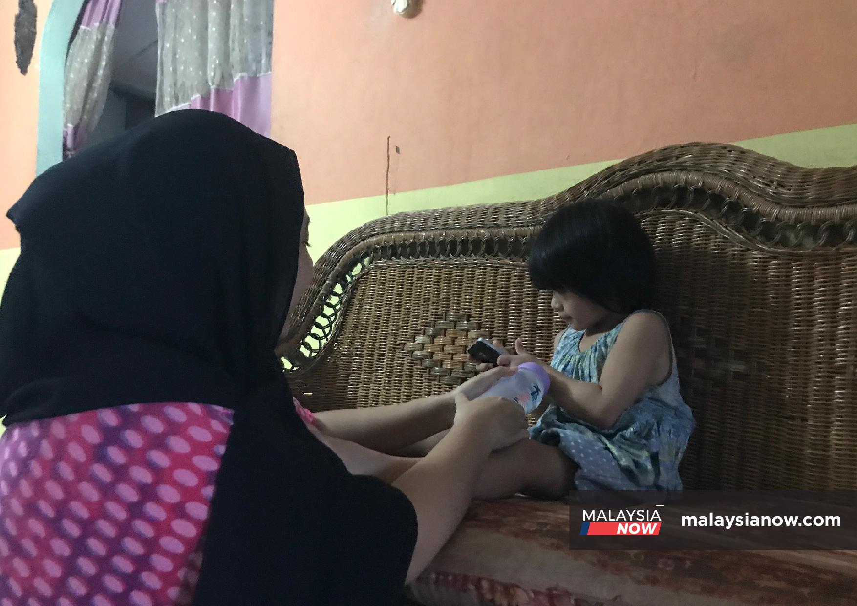 Nurul Fariha Abdullah holds a bottle of milk as she coaxes her four-year-old sister to drink.