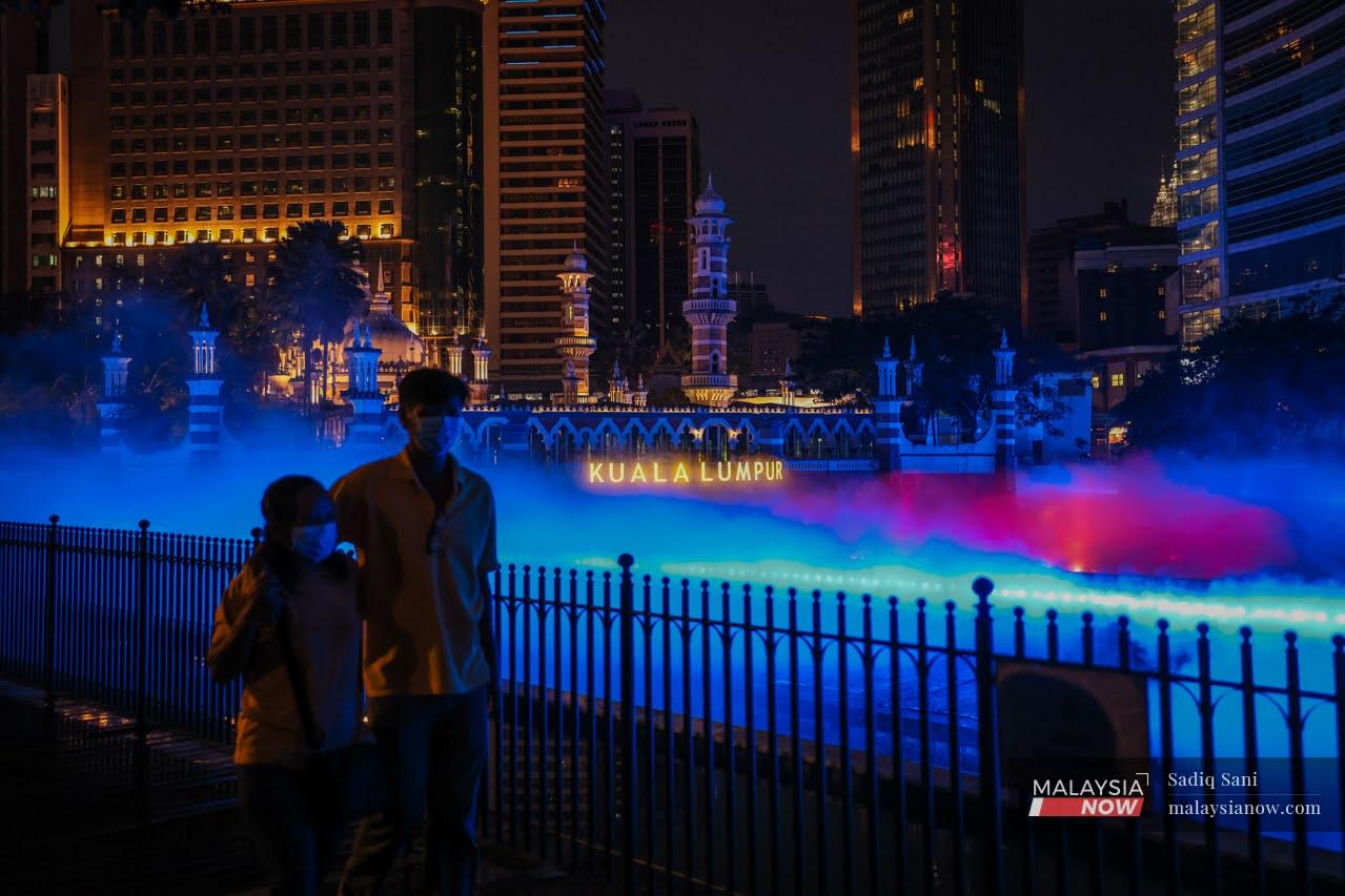 A couple strolls along the River of Life at Dataran Merdeka in Kuala Lumpur, which is lit up in blue.