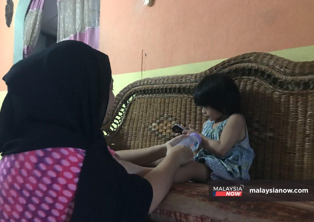 Nurul Fariha Abdullah melayani adik bongsunya di rumah di Kampung Penan Islam, Bintulu, Sarawak.