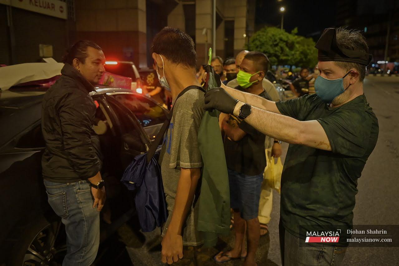 Sukarelawan membantu mengukur baju Melayu pada seorang lelaki gelandangan bandar yang berbaris untuk mendapatkan bantuan makanan dan baju Melayu bagi sambutan Aidilfitiri minggu depan.