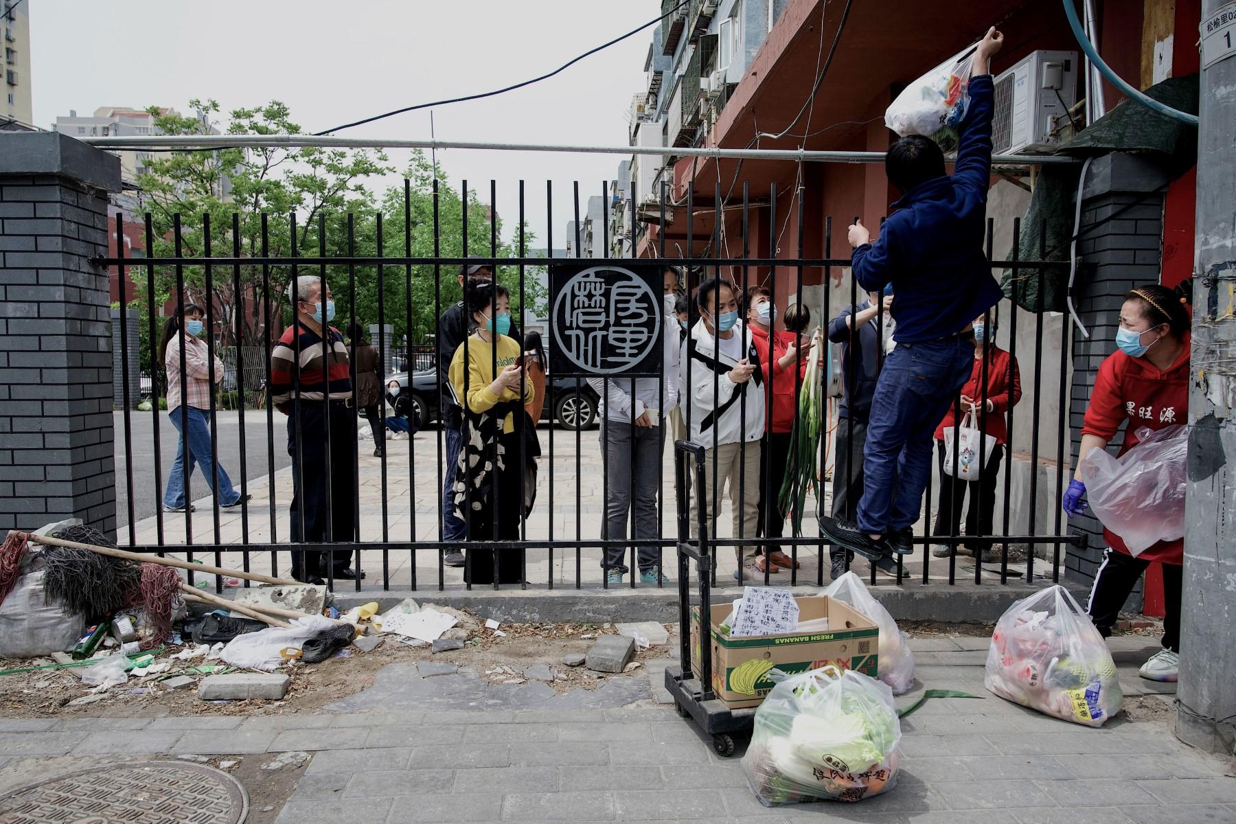 A delivery worker (right) passes items over a fence to people in a residential area under lockdown due to Covid-19 restrictions in Beijing on May 9. Photo: AFP