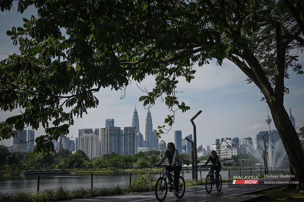 Visitors cycle along a path in Taman Tasik Titiwangsa in Kuala Lumpur, as the Twin Towers loom in the background.