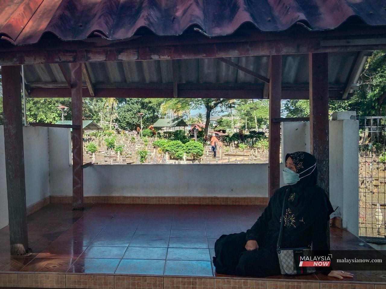 Kak Ma sits in a hut outside her parents' cemetery in her home town of Rantau Panjang, Kelantan.