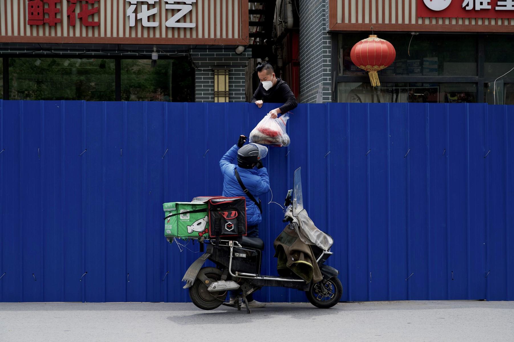 In this file photo taken on May 11, a delivery worker passes items to a man inside a fenced residential area under Covid-19 lockdown in Beijing. Photo: AFP
