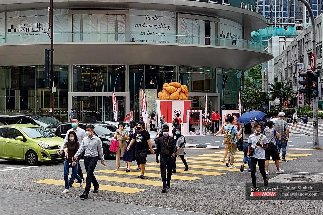 Pedestrians wearing face masks cross a road in the capital city of Kuala Lumpur.