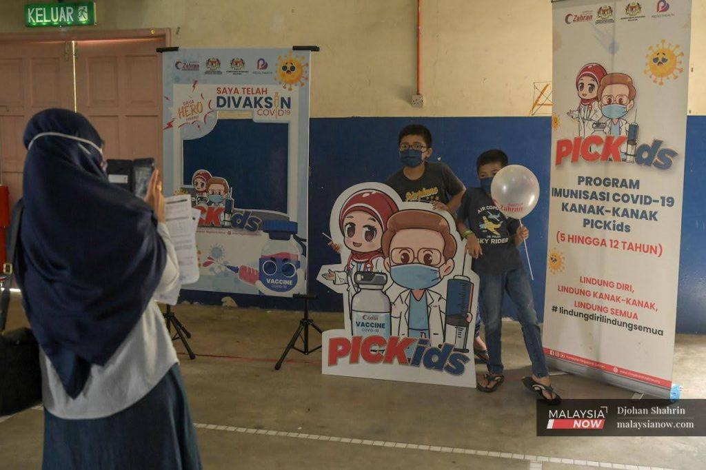 A woman snaps a picture of her newly vaccinated sons at the Dewan Komuniti Taman Bukit Mewah vaccination centre in Kajang.
