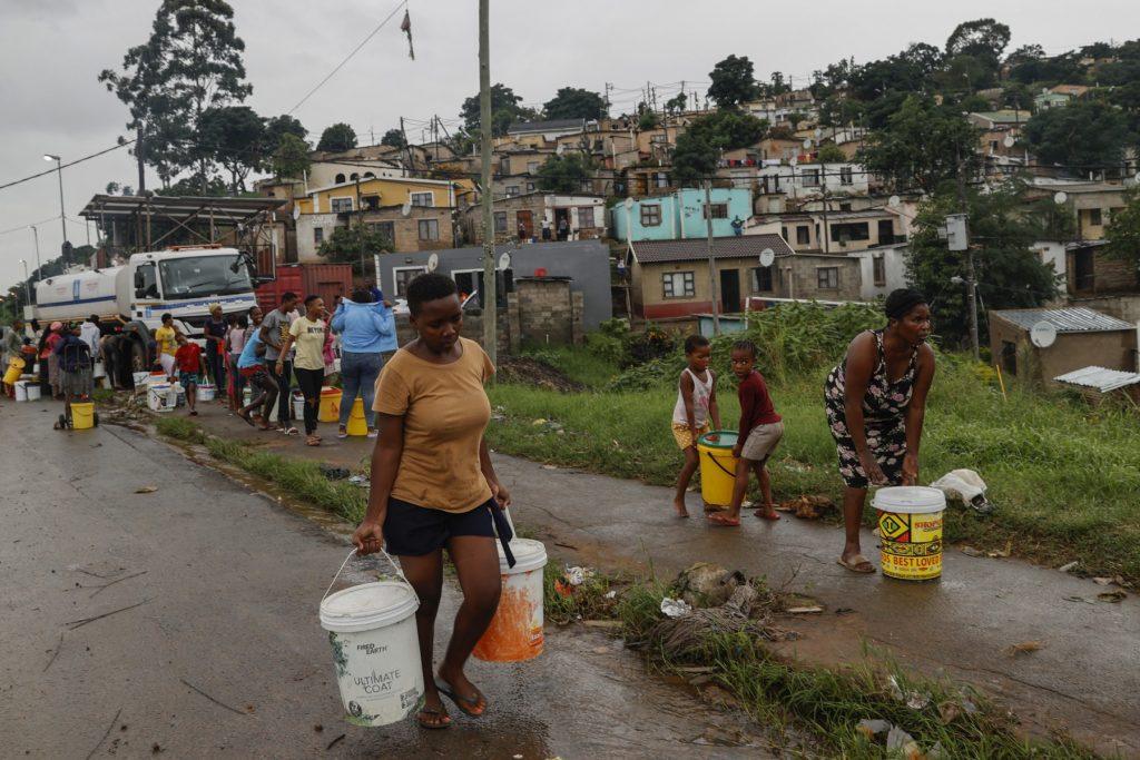 Residents of Bhambayi settlement walk with buckets filled with water after filling them form a water tanker as a result of interruptions by heavy rains and floods on the M25 highway in Inanda, north of Durban on April 13. Photo: AFP
