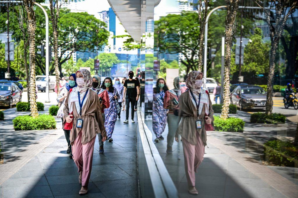 People wearing face masks walk past a building along a street in Kuala Lumpur. Photo: AFP