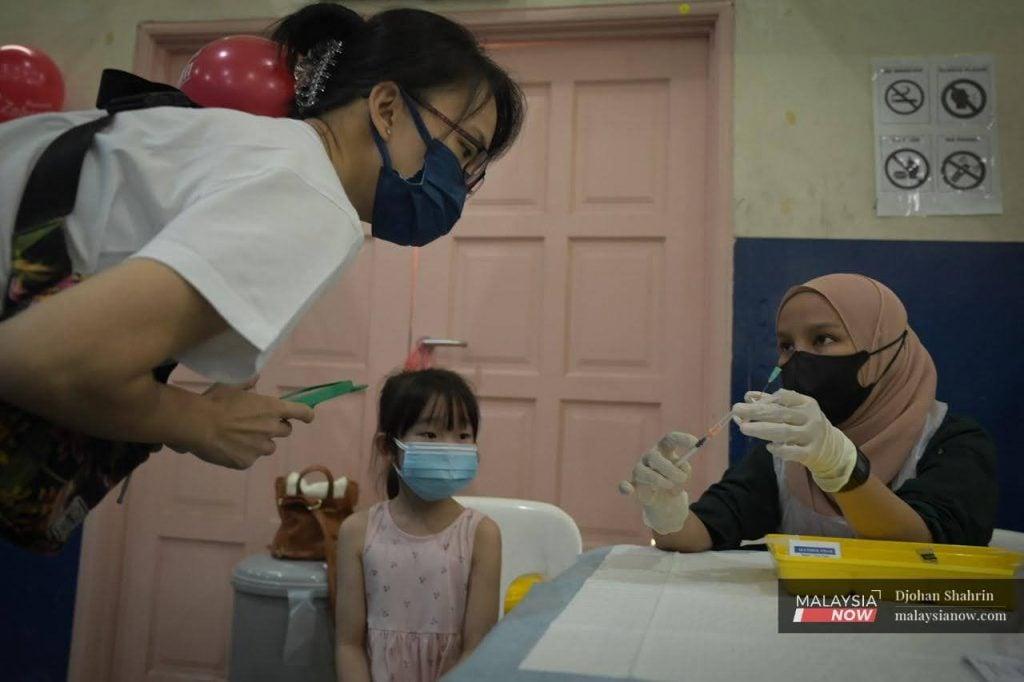 A health worker shows a syringe of Covid-19 vaccine to a woman before administering it to her child at the Dewan Komuniti Taman Bukit Mewah vaccination centre in Kajang.