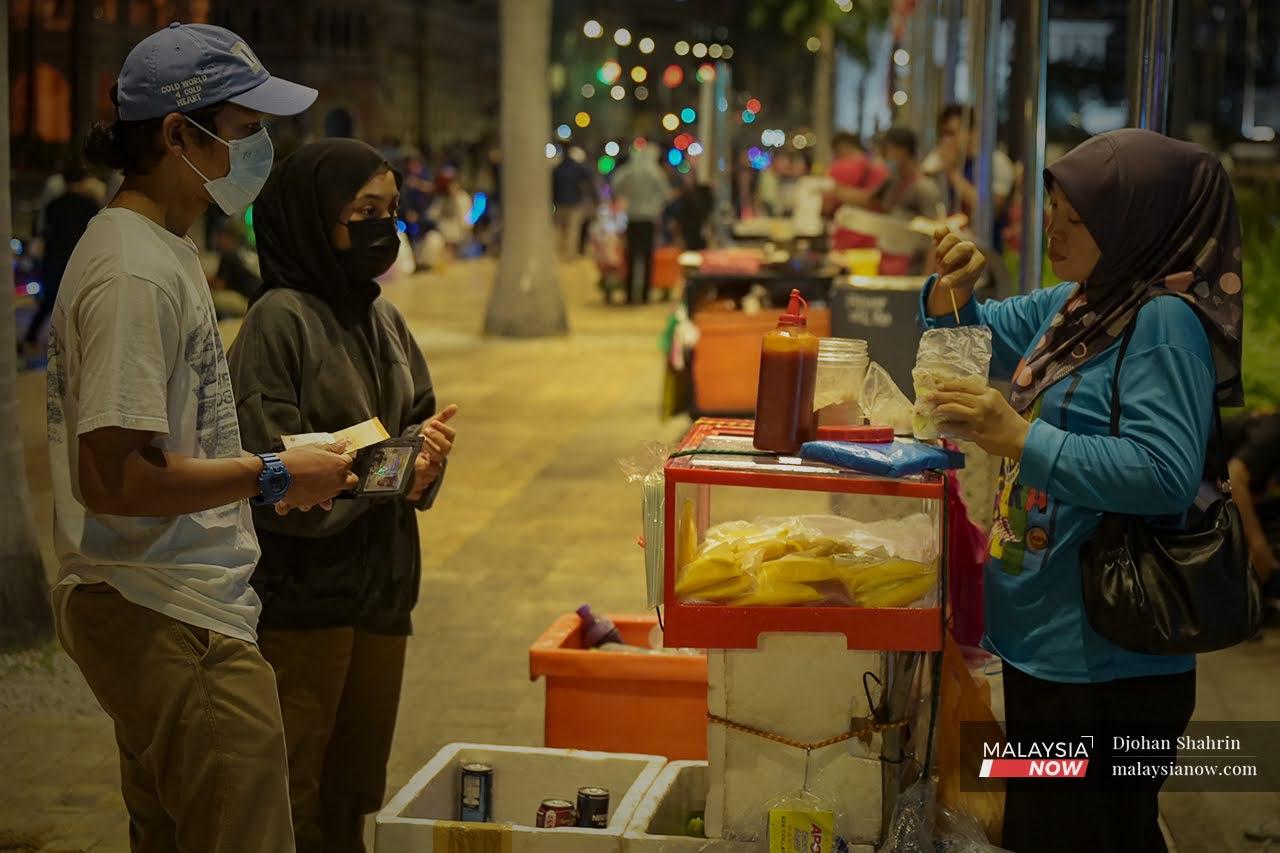 Pengunjung Dataran Merdeka membeli snek buahan-buahan ketika bersiar-siar di lokasi tarikan pelancong di Kuala Lumpur itu.
