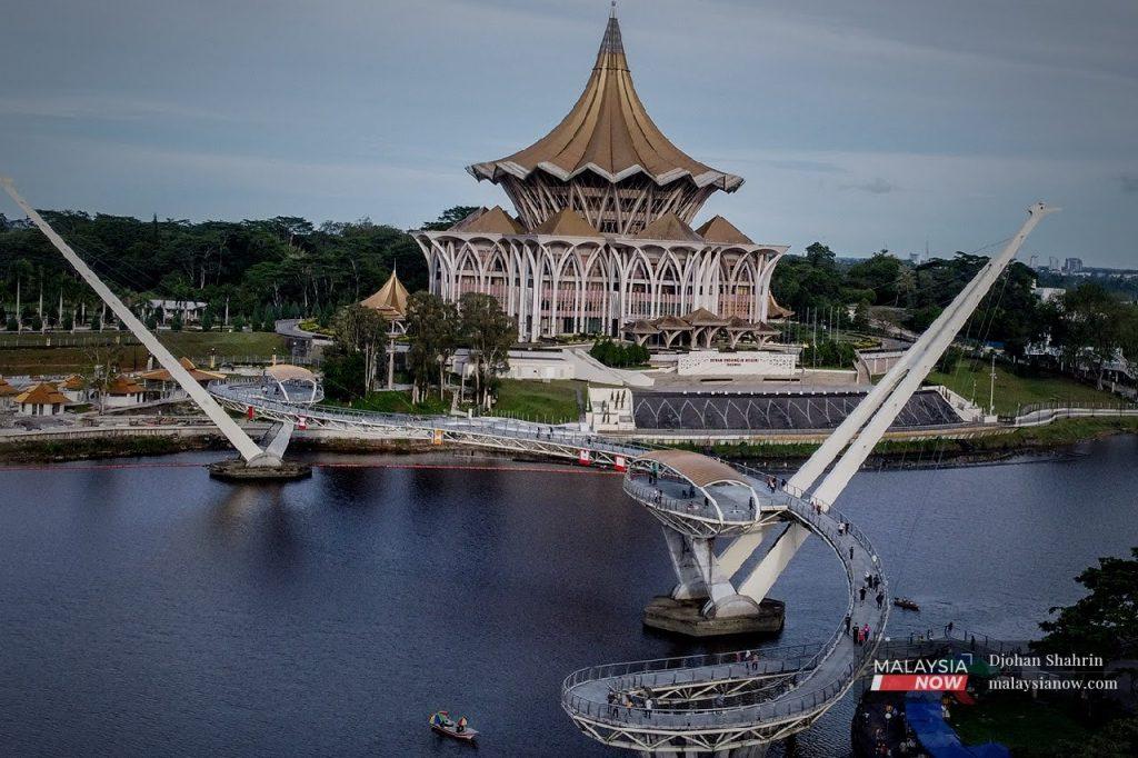 Pelancong menyeberangi jambatan Darul Hana di Waterfront, berhampiran bangunan Dewan Undangan Negeri di Kuching, Sarawak.