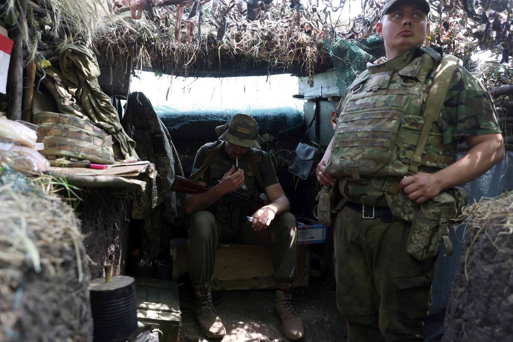 A Ukrainian serviceman smokes a cigarette as another looks on in an entrenched position on the front line near Avdiivka, Donetsk region on June 18. Photo: AFP