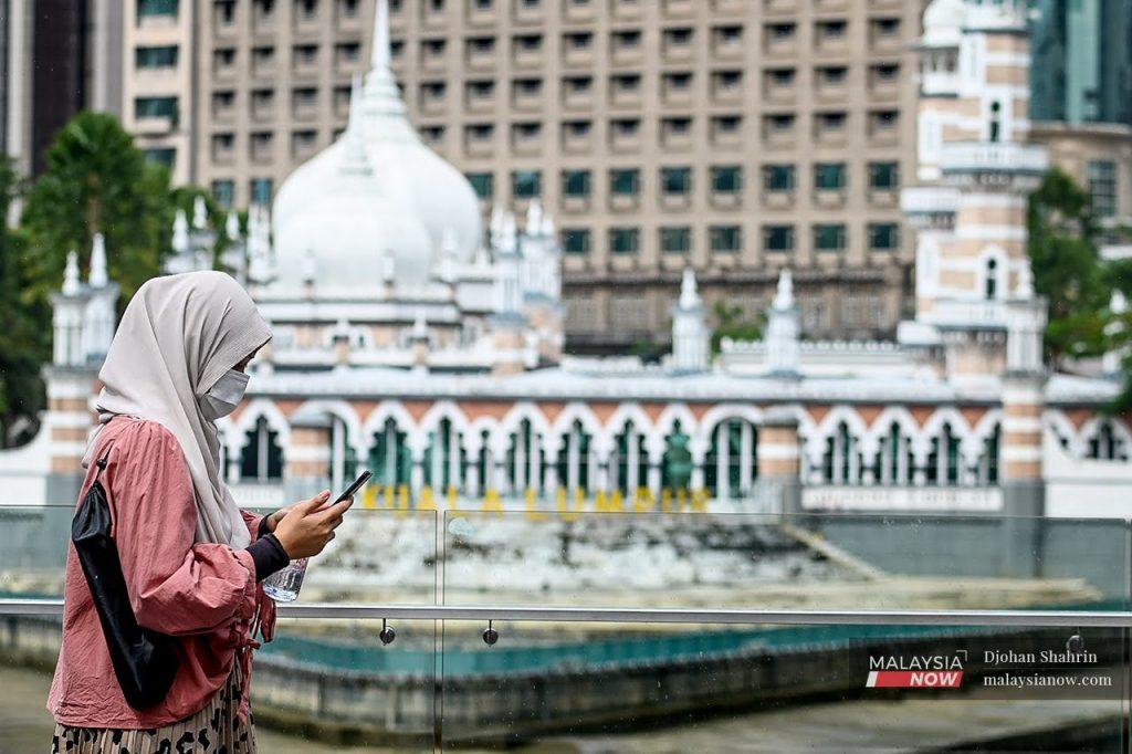 Seorang wanita melihat telefon pintarnya ketika berjalan melalui Masjid Jamek di Kuala Lumpur.