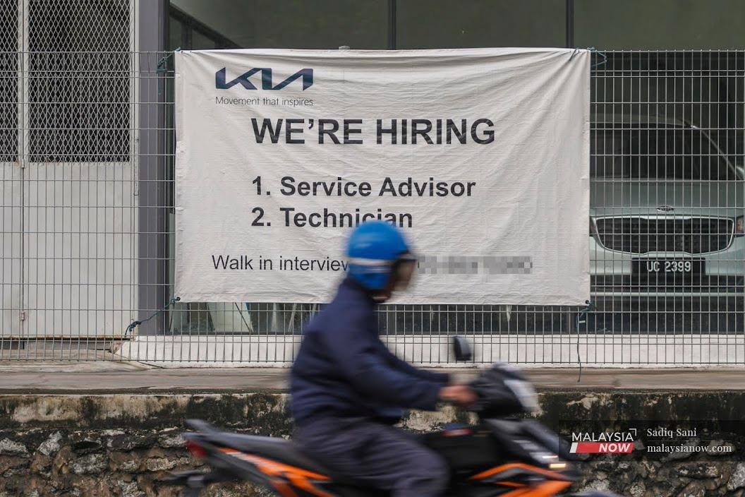 Seorang penunggang motorsikal melalui iklan jawatan kosong yang digantung di Bangi, Selangor.