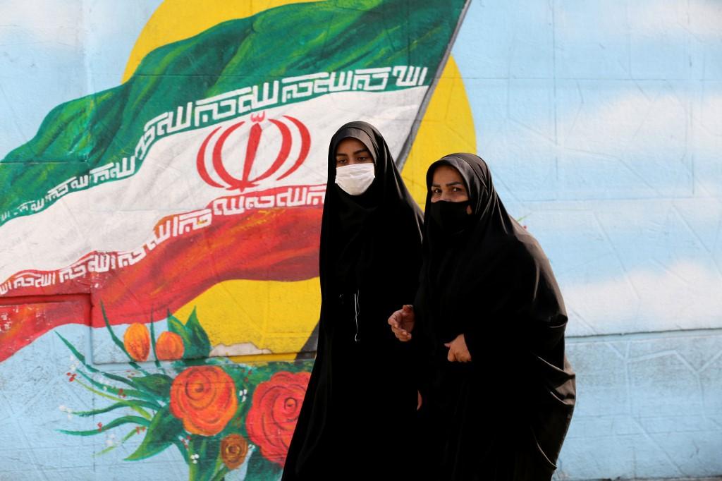 Dua wanita memakai pelitup muka ketika berjalan di bandar Tehran melalui mural bendera Iran. Gambar: AFP