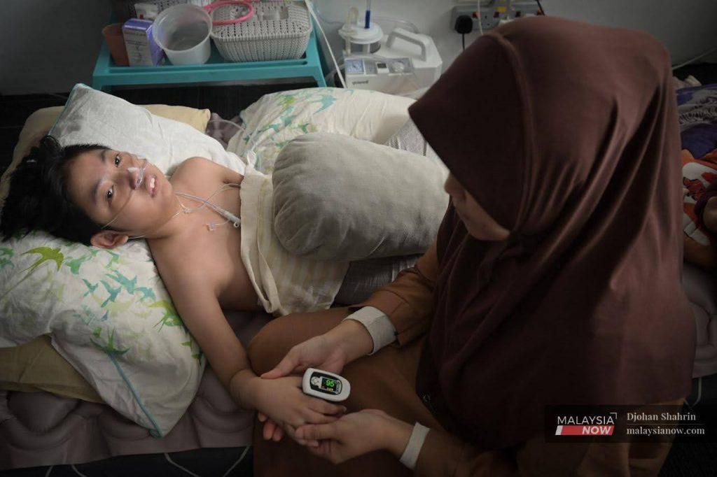 Zaitul Akma Muhd Zin checks her daughter's oxygen level during a MalaysiaNow visit in April. At that point, Aliya Darwisyah could no longer move, see, hear or speak.