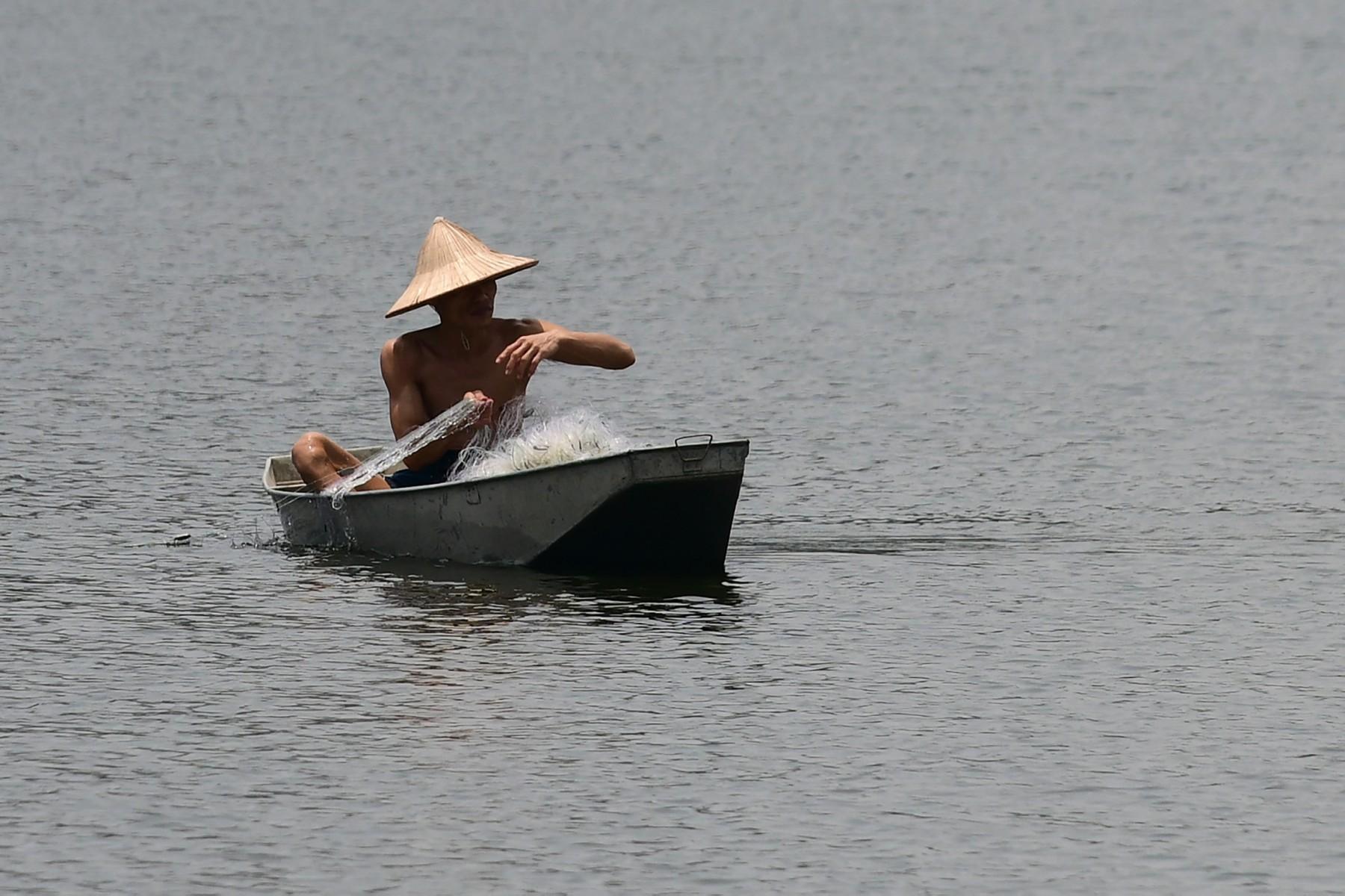 A fisherman works to catch fish on Truc Bach lake in Hanoi on May 11, 2021. Photo: AFP