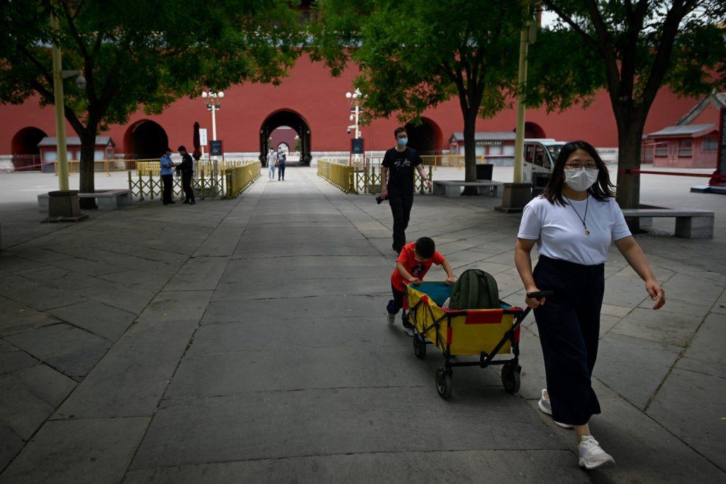 A woman pulls a portable cart with a child pushing back as they prepare to visit the Forbidden City in Beijing on June 7. Photo: AFP