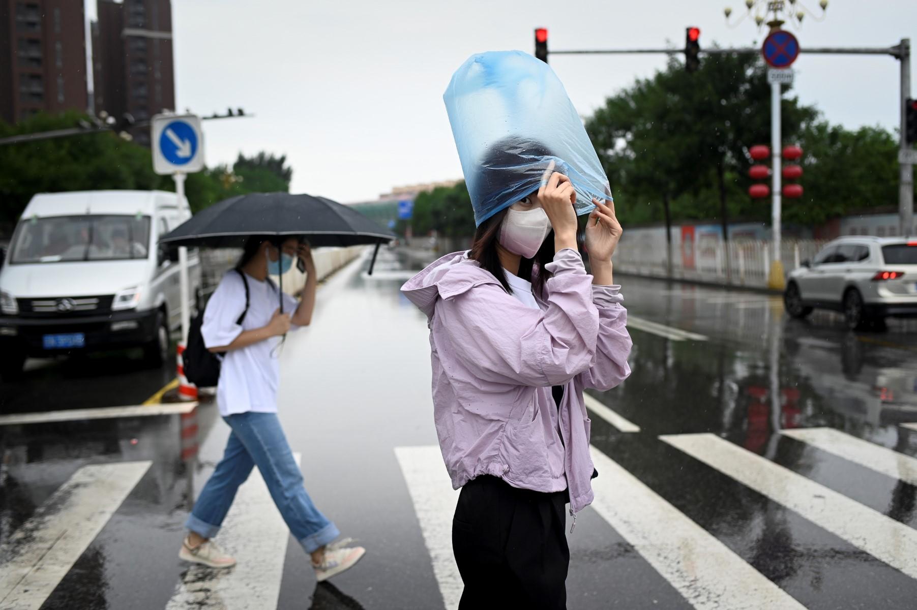 A woman uses a plastic bag to shelter from the rain as she crosses a street in Beijing on June 27. Photo: AFP