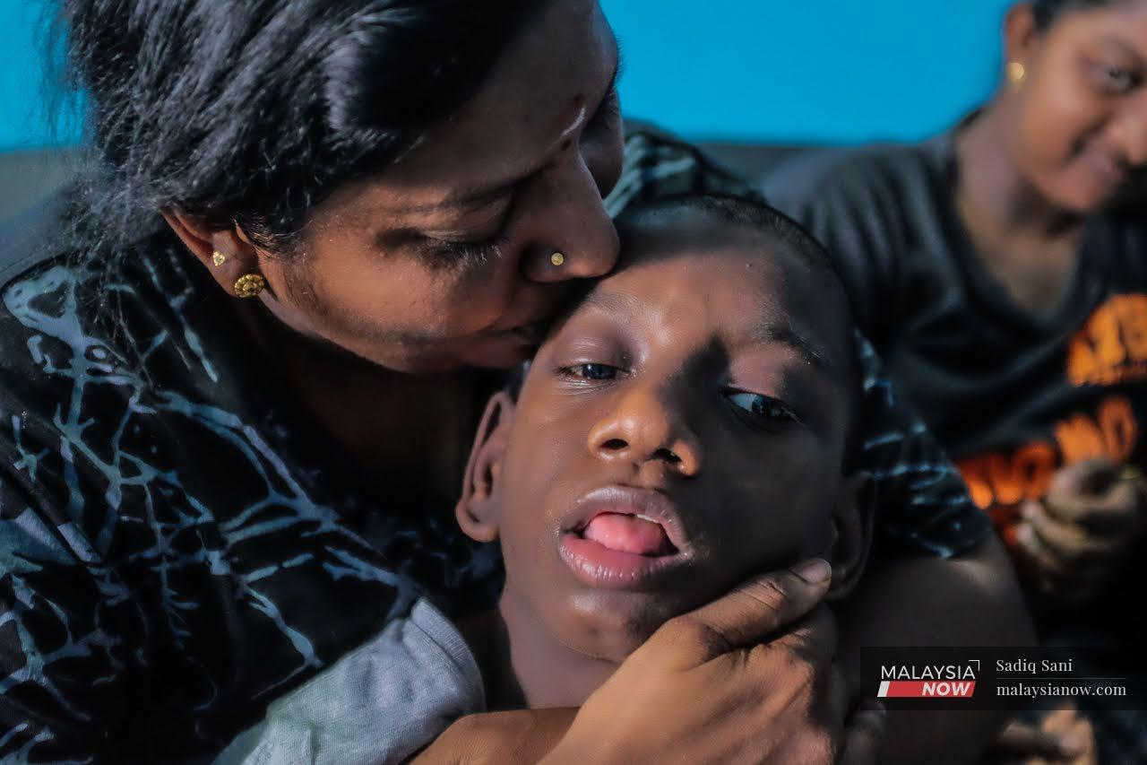 K Goomathi gives her son, K Thiviyan, a kiss on his forehead as her daughter K Daarshini smiles beside her at their house in Sungai Petani, Kedah.